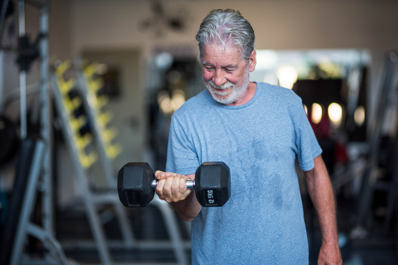 An elderly man workout in a fitness club with dumbbells in his hand